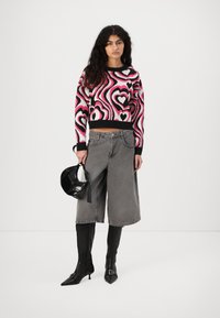 Maglione corto a fantasia cuori nero e rosa, pantaloni di jeans ampi grigi, stivali neri alti fino al ginocchio e una piccola borsa nera.
