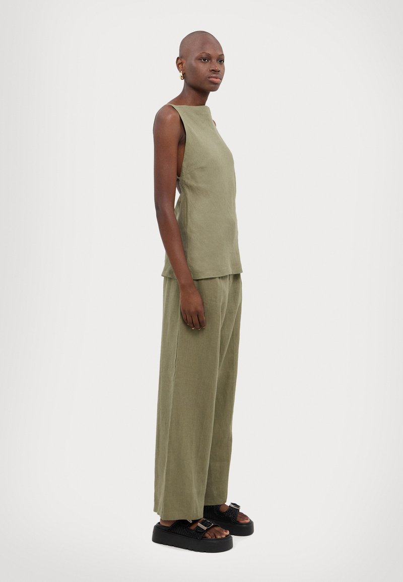 Top senza maniche verde oliva abbinato a pantaloni larghi coordinati. Entrambi realizzati in un tessuto leggero e strutturato. Sandali neri e spessi.