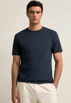 Sügav sinine lühikeste varrukatega T-särk, mis on valmistatud siledast kangast, meeskonnakaelusega ja regulaarse lõikega, koos heledate pükstega.