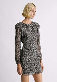 Vestido de estampado en blanco y negro con mangas largas y transparentes, y un escote con volantes. Presenta una silueta ajustada y detalles de dobladillo con volantes.