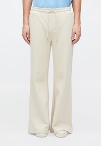 Pantalones de chándal beige de corte holgado, con cinturilla elástica, cordón ajustable y bolsillos laterales. Tejido suave con una textura lisa.