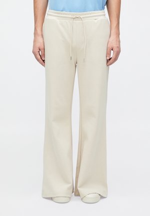 Pantaloni tuta beige con una vestibilità ampia, vita elasticizzata, cordoncino e tasche laterali. Tessuto morbido con una texture liscia.