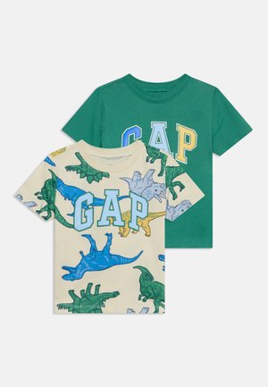 Deux t-shirts à manches courtes pour enfants, un vert avec des lettres GAP multicolores, et un beige avec un motif dinosaure et des lettres GAP.