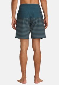 Herren Badehose in dunkeltürkis mit horizontalen beigen Streifen. Sie hat einen flachen Bund, Gesäßtaschen und eine leichte, glatte Stoffstruktur.