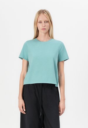 Cropped, T-shirt met korte mouwen van teal katoen. Voorzien van een ronde halslijn en zijsplitten. Gepaard met losse zwarte broek.