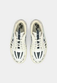 Pár bielych tenisiek Nike Air s čiernymi a sivými detailmi, šnúrky uviazané, zobrazené zhora na bielom pozadí.
