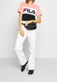 En rosa, svart och vit färgblockerad Fila t-shirt ihop med vita vida byxor. Svart bältesväska och svarta sneakers fulländar outfiten.