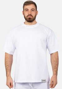 T-shirt bianco a maniche corte realizzato in tessuto leggero, con colletto rotondo e un'etichetta sull'orlo con il nome del marchio.