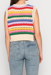 Donna vista da dietro che indossa un gilet in cotone senza maniche con righe orizzontali multicolori e jeans leggeri a vita alta di colore blu.