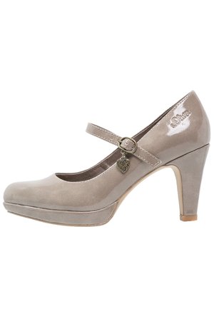 Chaussure Mary Jane en cuir verni beige avec un bout rond, une sangle à la cheville, un charm en métal en forme de cœur et un petit talon aiguille. Texture de surface lisse.