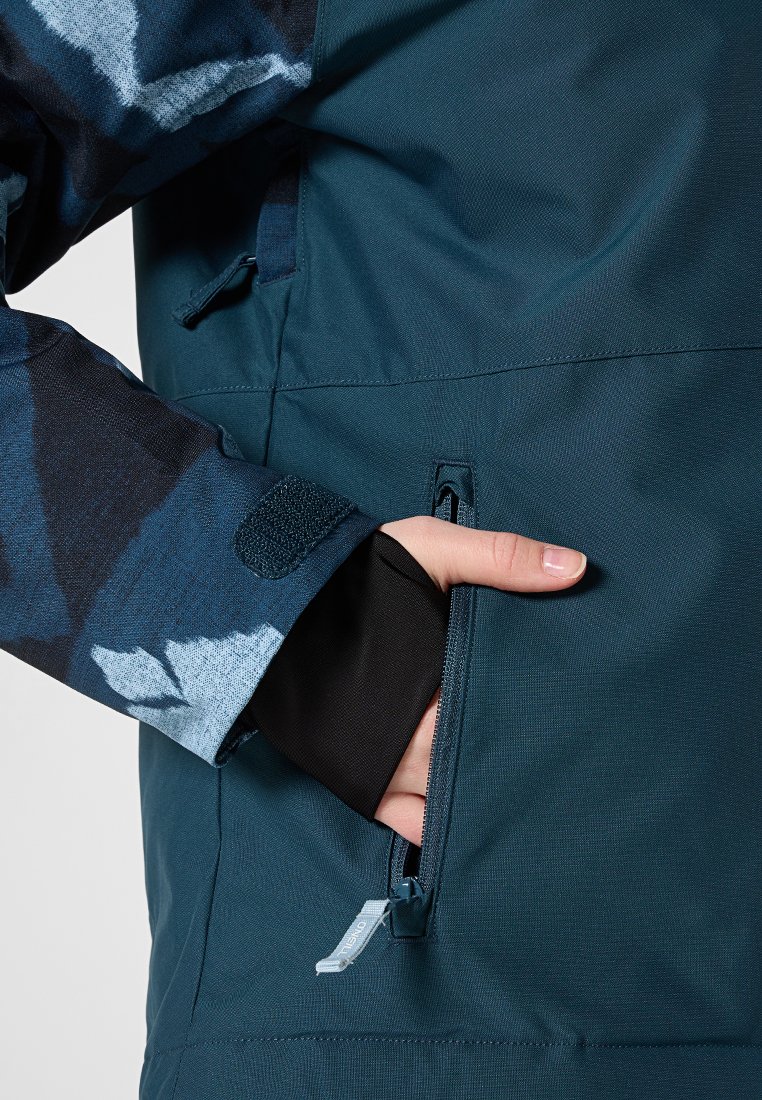 Türkise, wasserdichte Jacke mit gemustertem Ärmel, Reißverschluss-Tasche und Klettverschluss am Bündchen. Das Material hat eine glatte Textur und verfügt über ein Logoschild.