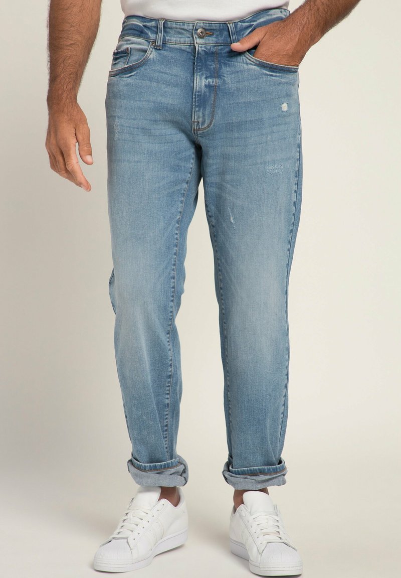 Jeans de mezclilla azul claro con un ajuste relajado, ligero desgaste, diseño clásico de cinco bolsillos y puños enrollados, combinados con zapatillas blancas.