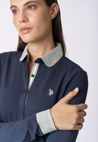 Polo navy con colletto e polsi grigi, dotato di logo ricamato sul lato sinistro del petto e chiusura con bottoni. Texture morbida.