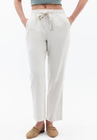 Pantalones de lino de color beige claro con cintura elástica, cordón y bolsillos laterales. La tela tiene un acabado texturizado y piernas de corte recto.
