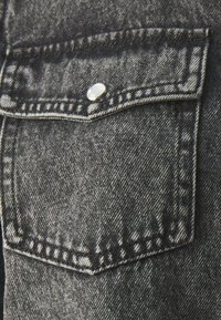 Zwart denim zakje met een zilveren drukknoop, voorzien van contrasterende witte stiksels en een geweven, gestructureerde stof.