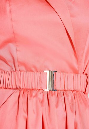 Koraalroze kledingstuk met een geplooide tailleband met een rechthoekige zilveren gesp in het midden.