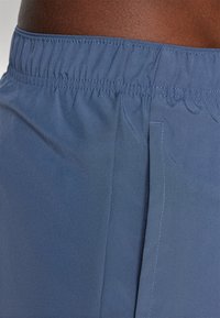 Navy blue shorts dengan pinggang elastis yang halus, memiliki tekstur yang mulus dan jahitan samping, menampilkan kilau yang lembut tanpa pola atau perangkat keras yang terlihat.