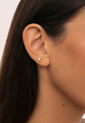 Pendiente de stud en forma de pájaro dorado, con alas detalladas y un diseño elegante. Se lleva en el lóbulo de la oreja, complementando los contornos naturales de la oreja.
