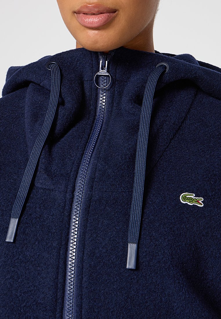 Navyblaue Fleece-Zip-Hoodie mit großer Kapuze, Zugbändern, silbernem Reißverschluss und kleinem gesticktem Alligator-Logo auf der Brust.