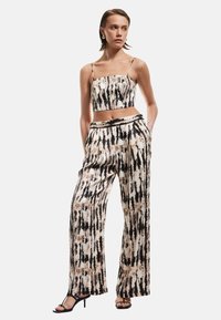 Ensemble deux pièces comprenant un haut court et un pantalon à jambes larges. Le tissu présente un motif tie-dye noir et beige ; texture lisse ; design simple.
