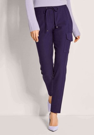 Marineblaue Hose mit Kordelzug, Seitentaschen und schmaler Passform. Glatter Stoff mit leichtem Glanz, kombiniert mit lavendelfarbenen High Heels.