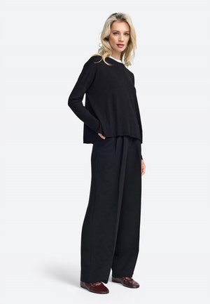 Maglione nero a maglia con una vestibilità ampia e maniche lunghe, abbinato a pantaloni neri a gamba larga e scarpe scure. Design semplice e coerente.