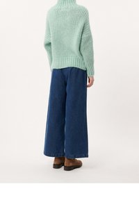 Ljusgrön oversized stickad tröja med hög krage, tillsammans med vida blå denimbyxor och bruna ankelstövlar.