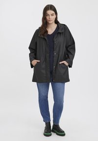 Black waterproof jacket with a hood, snap buttons, and two front pockets. Paired with blue jeans and black boots with green accents.