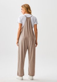 Brauner, locker sitzender Overall aus weichem Stoff mit dünnen Trägern und entspannter Silhouette, kombiniert mit weißem T-Shirt und weißen Schuhen.