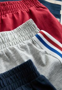 Vier Paare von Shorts mit elastischem Bund in Rot, Grau, Marine und mit gestreiftem Saum. Aus weichem Baumwollmaterial mit glatter Textur.