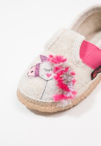 Chausson en feutre avec un design de licorne rose et blanche, mettant en avant des accents de fil texturé et une sangle élastique rose. Bout fermé, base beige clair.