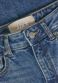 Jeans aus Denim mit einem hellblauen Waschung, sichtbaren Nähten in Orange, einem Metallknopf mit eingraviertem Logo und einem Stoffetikett mit der Aufschrift "JJXX."