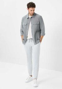 Gray button-up jacket with two chest pockets, over a white t-shirt, paired with light gray joggers and white sneakers, set against a plain background.
