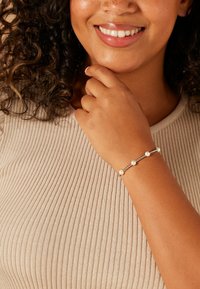 Zilveren armband met ronde witte parels, afgewisseld met kleine zilveren kralen. De hand van het model rust op de kin en toont het ontwerp van de armband.