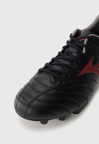Black leather football cleat featuring textured stripes, black laces, and red accents. Designed for traction with visible studs on the sole.