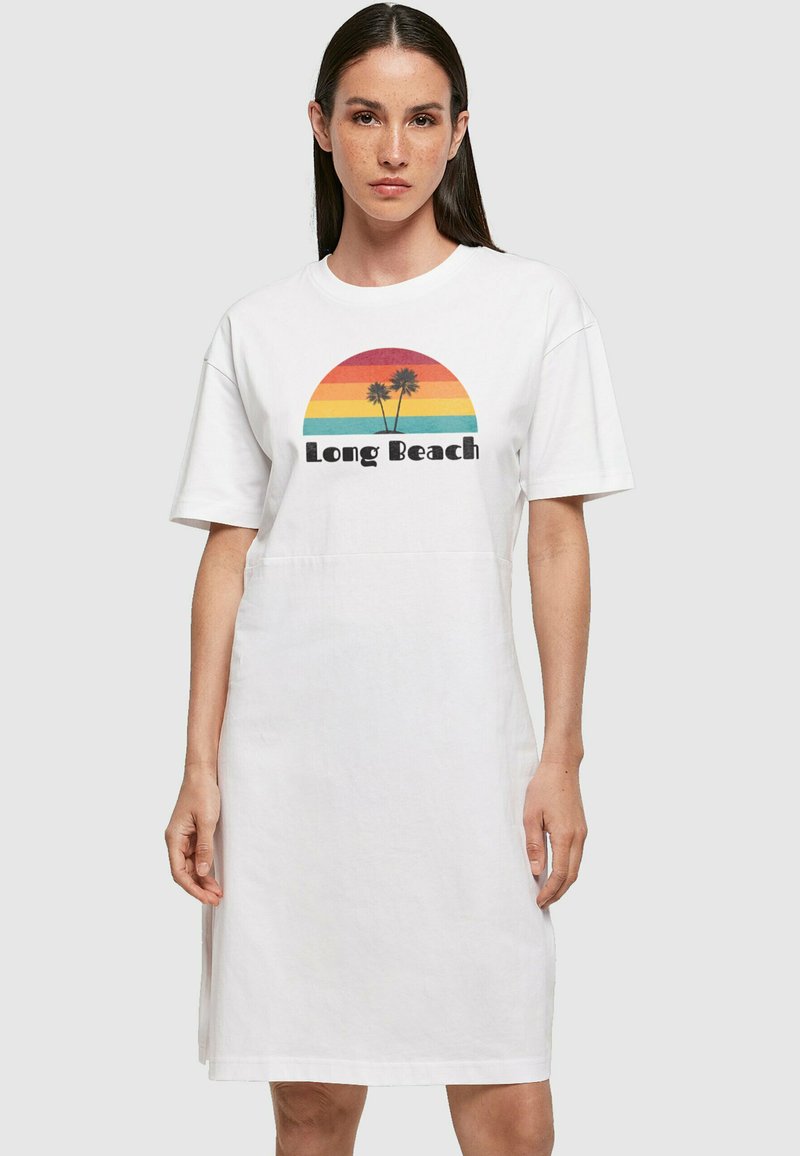 Weißes Kurzarmkleid mit einem bunten Grafikdesign von einem Sonnenuntergang und Palmen, mit dem Text "Long Beach" in Schwarz. Lässige, entspannte Passform.