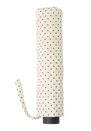 Parapluie blanc fermé à pois noirs avec une sangle en tissu assortie, debout verticalement sur un fond blanc.