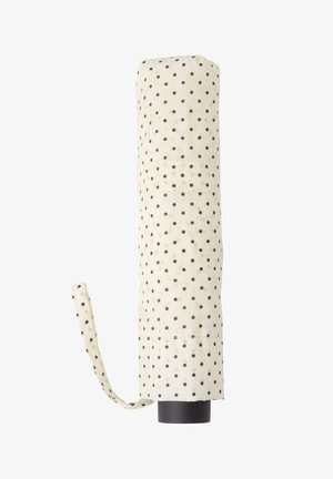 Parapluie blanc fermé à pois noirs avec une sangle en tissu assortie, debout verticalement sur un fond blanc.