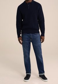 Marinblå stickad tröja med polokrage och tre knappar, tillsammans med blå jeans och mörka sneakers. Mjuk textur, avslappnad passform och ledig stil.