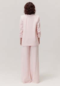 Różowy garnitur z długim żakietem o gładkiej fakturze oraz spodniami z szerokimi nogawkami. Zaprojektowany w minimalistycznym stylu, bez widocznych detali.