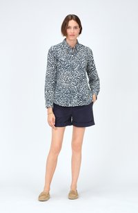 Camisa de manga larga a rayas en azul marino y blanco con cierre de botones, combinada con pantalones cortos azul marino y zapatos de tela beige. Diseño sencillo, ajuste casual.