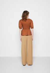Top em bege com mangas bufantes e franzido, combinado com calças largas de tom beje claro. Tecido suave, caimento solto e decote elegante.