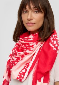 Écharpe à motifs rouge et blanc avec une texture douce, présentant des bords frangés et un design audacieux. Forme rectangulaire drapée autour du cou.