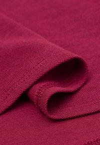 Burgunderfarbener Stoff mit strukturierter Oberfläche, der eine weiche, umgeschlagene Kante und eine saubere Naht entlang des Saums zeigt.