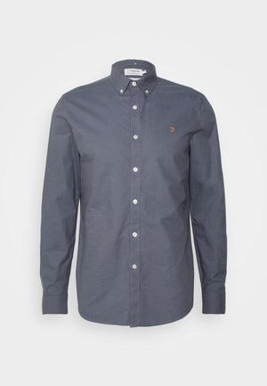 Donkergrijs overhemd met knopen, kraag, lange mouwen en een klein gouden logo op de borst. Heeft witte knopen en een gladde stoftextuur.