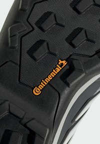 Suola di calzature nera con profondi modelli di trazione, superficie testurizzata e un accento bianco sul bordo. Presenta un logo "Continental" arancione.