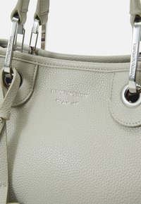 Ljust grått texturerat läderhandtag med silverfärgad hårdvara och präglad Emporio Armani Milano 1981-logotyp framtill.