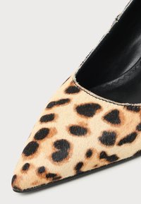 Gros plan sur une chaussure à bout pointu avec un motif léopard et une doublure intérieure noire sur un fond clair.