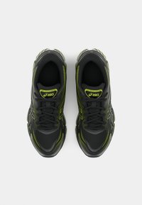 Črne športne čevlje z neonsko zelenimi poudarki, z strukturirano zgornjim delom, vezalkami in oblazinjeno podplati za podporo.