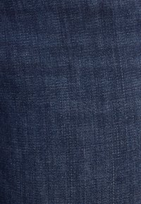 Denim tyg i mörkblått med en subtil, strukturerad väv. Har en enhetlig färg med små variationer och ljusa stickningsdetaljer.